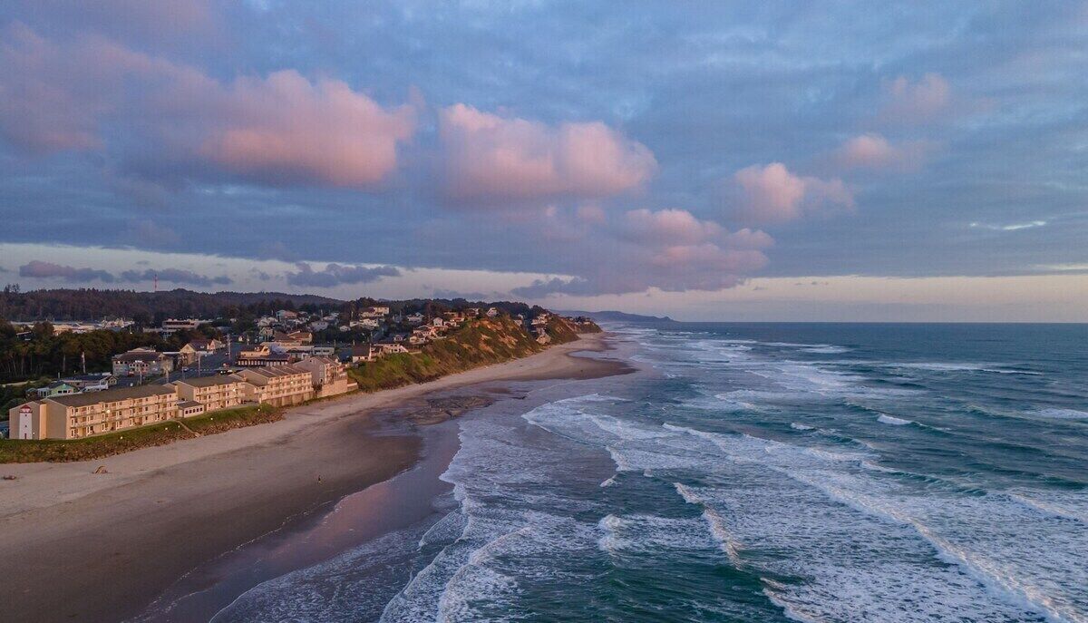Une ville côtière avec un hôtel en bord de mer, des vagues de l’océan et un ciel nuageux.