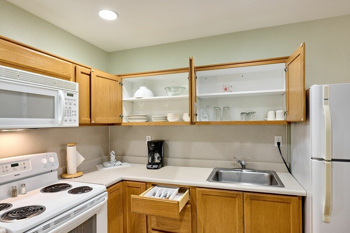 A kitchen with wooden cabinets, a microwave, a stove, a sink, and a refrigerator.