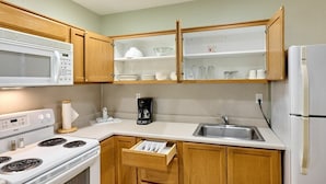 A kitchen with wooden cabinets, a microwave, a stove, a sink, and a refrigerator.