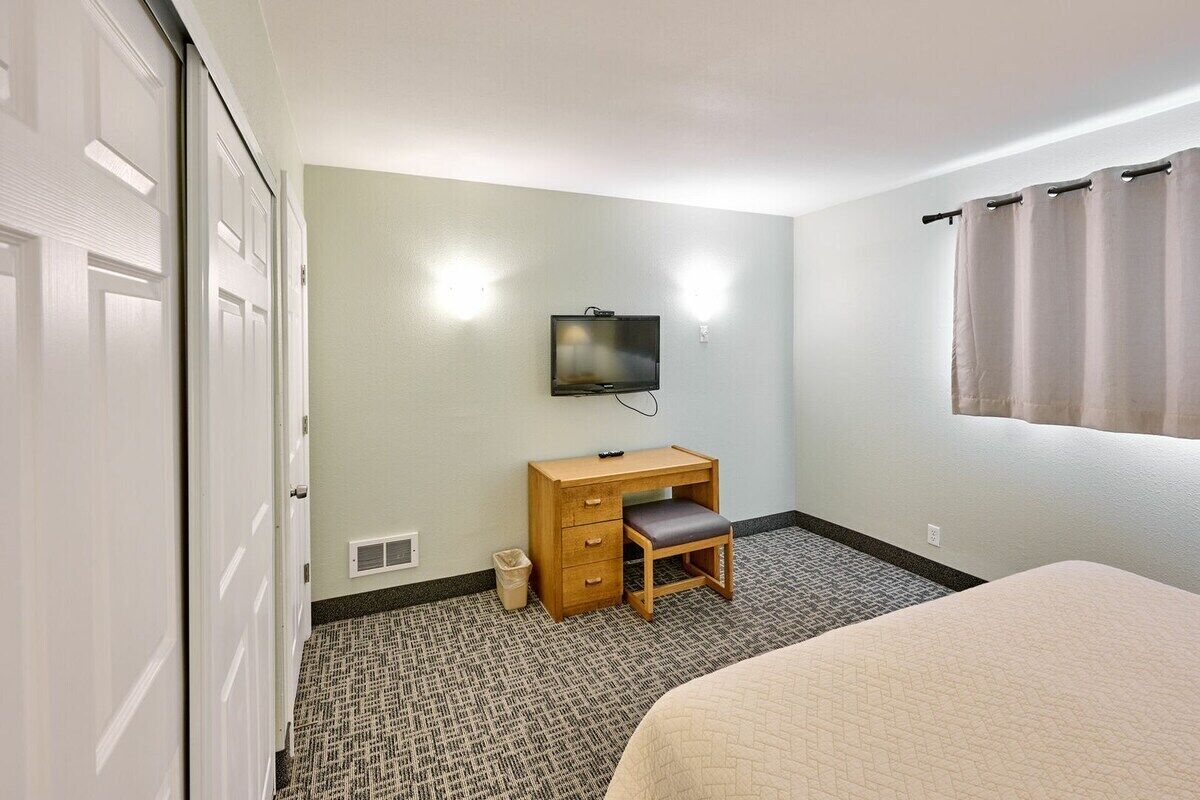Une chambre d’hôtel avec un lit, un bureau et une chaise, une télévision et une fenêtre avec des rideaux.