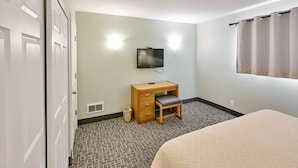 A hotel room with a bed, a desk with a chair, a television, and a window with curtains.
