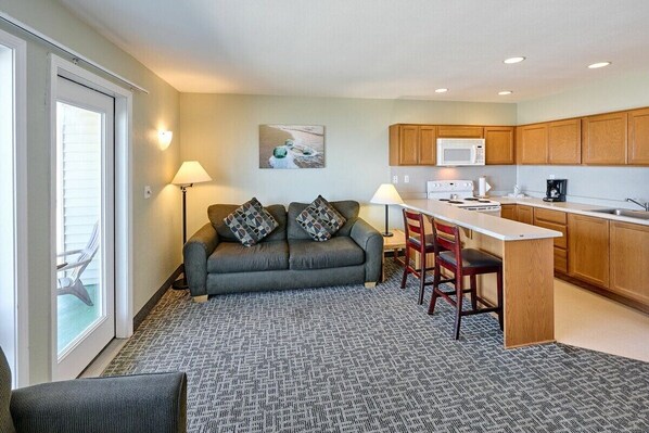 A compact living space with a sofa, chairs, a small kitchen area, and a sliding glass door leading to an outdoor area. - Oceanfront Suite - Beach Access - Heated Pool and Hot Tub! (Lincoln City)