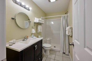 A bathroom with a round mirror, a sink with toiletries, a toilet, and a shower area. - Oceanfront Suite - Beach Access - Heated Pool and Hot Tub! (Lincoln City)