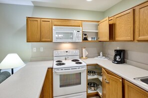 A compact kitchen with wooden cabinets, a white stove, and a microwave. - Oceanfront Suite - Beach Access - Heated Pool and Hot Tub! (Lincoln City)