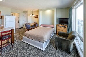 A hotel room with a bed, a desk with a chair, a television, and a window with curtains. - Oceanfront Suite - Beach Access - Heated Pool and Hot Tub! (Lincoln City)