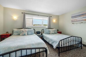 Une chambre avec deux lits simples, une fenêtre avec des rideaux, une lampe fixée au mur, une petite table et une chaise.