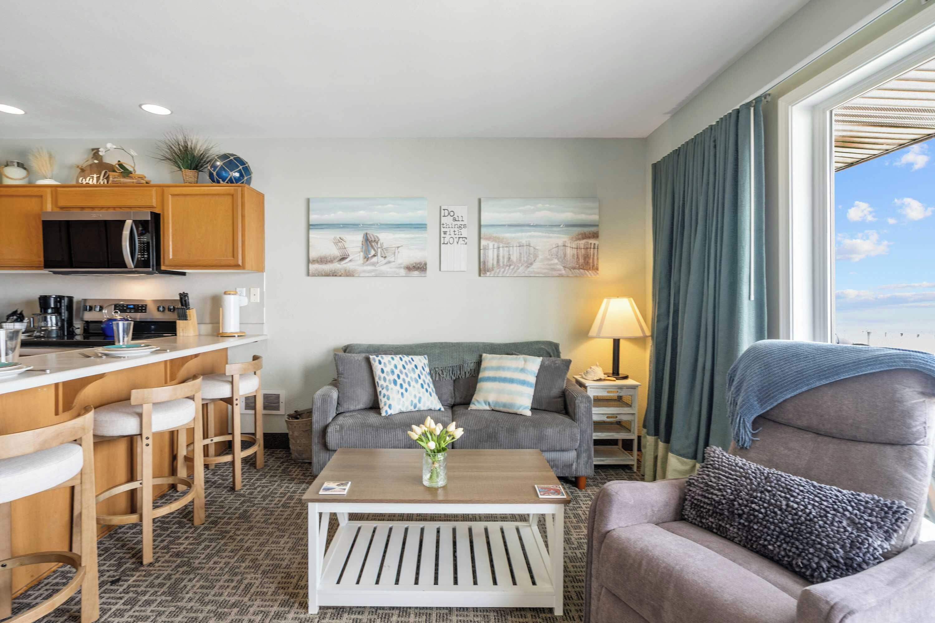 Ein modernes Hotelzimmer mit Küchenzeile, einer Sitzecke mit Sofa und Sesseln, einem Couchtisch und Blick auf den Ozean.