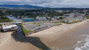 An aerial view of a coastal town with a beach, a parking lot, and buildings including a blue hotel.