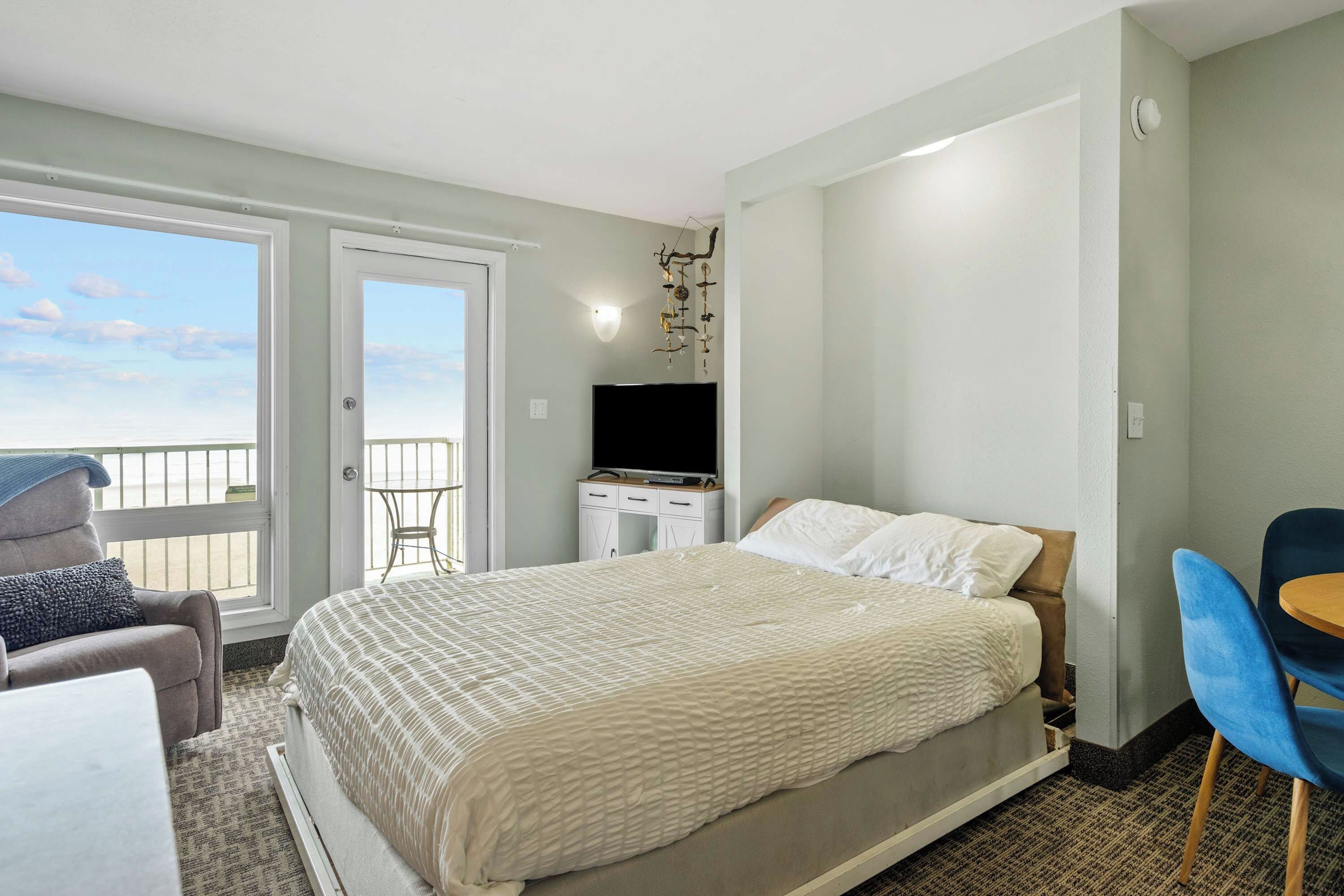 Une chambre avec un lit, un bureau avec une télévision, une chaise et un balcon.