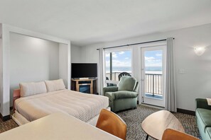 A hotel room with a bed, a TV, a balcony with a chair, and a table. - Oceanfront Suite - Sleeps Six - Full Kitchen - Pool and Hot Tub! (Lincoln City)