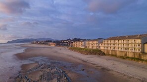 A coastal hotel with multiple floors, a sandy beach in the foreground, and a rocky shoreline.