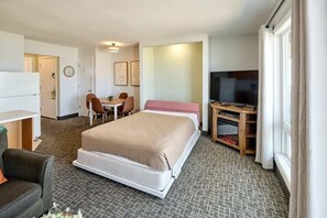 A hotel room with a bed, a desk, a chair, a television, and a window.