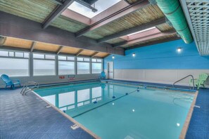 An indoor swimming pool with clear windows, blue and green chairs, and a blue and white wall.
