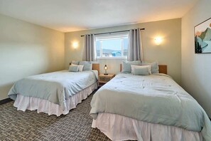 Quarto de hotel com duas camas de solteiro, uma janela com cortinas, uma luminária na parede e um quadro.