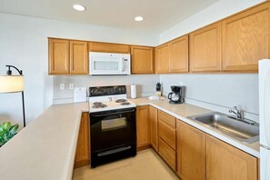 A modern kitchen with wooden cabinets, a white microwave, a black stove, and a stainless steel sink.