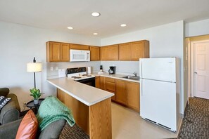 A compact kitchen with wooden cabinets, a white refrigerator, a microwave, and a stove. - Oceanfront Suite - Sleeps Six - Full Kitchen - Pool and Hot Tub! (Lincoln City)