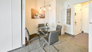 Un espace repas moderne avec une table en verre, des chaises grises et un tableau accroché au mur.