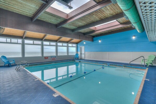 Una piscina interior con ventanas transparentes, sillas azules y una pared azul.
