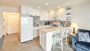 Une cuisine moderne avec des meubles blancs, un îlot central doté de sièges, un four à micro-ondes et une machine à café.