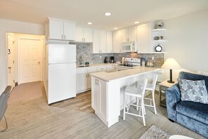 Una cocina moderna con armarios blancos, una isla central con asientos, microondas y cafetera.