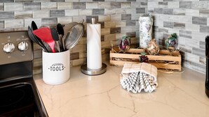 A kitchen counter with a utensil holder, a paper towel dispenser, and a wooden crate with jars and a cloth.