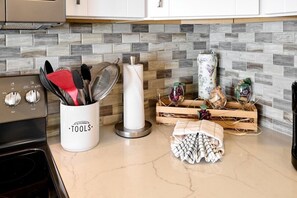A kitchen counter with a utensil holder, a paper towel dispenser, and a wooden crate with jars and a cloth.