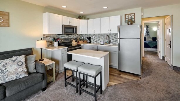A compact kitchen with white cabinets, a microwave, a refrigerator, and a small island with stools.
