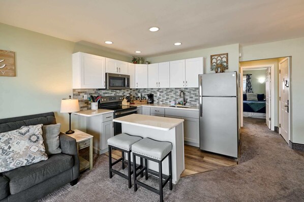 A compact kitchen with white cabinets, a microwave, a refrigerator, and a small island with stools.