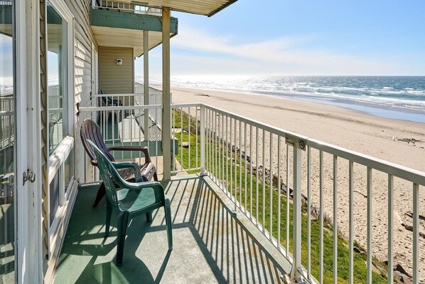 A beachfront property with a balcony, chairs, and a view of the ocean.