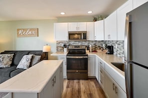 A modern kitchen with white cabinets, a microwave, an oven, and a refrigerator.