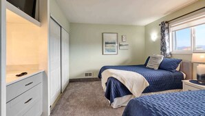 A bedroom with two beds, a wardrobe, a TV, and a window with curtains.
