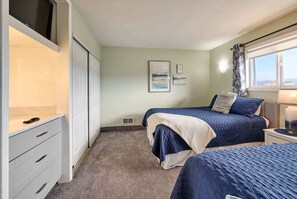 A bedroom with two beds, a wardrobe, a TV, and a window with curtains.