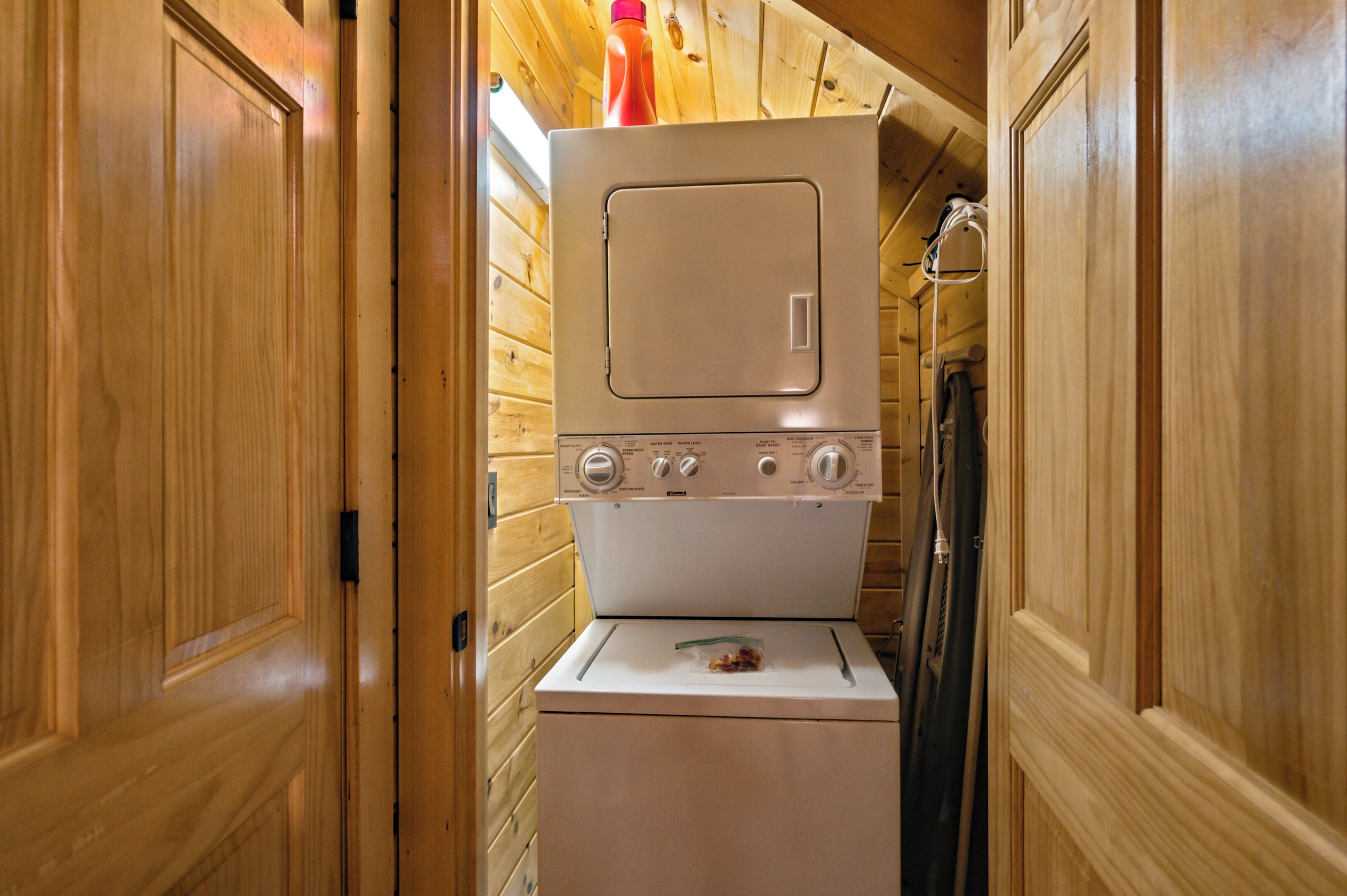 A compact laundry room with a washing machine and dryer, wooden walls, and a door.