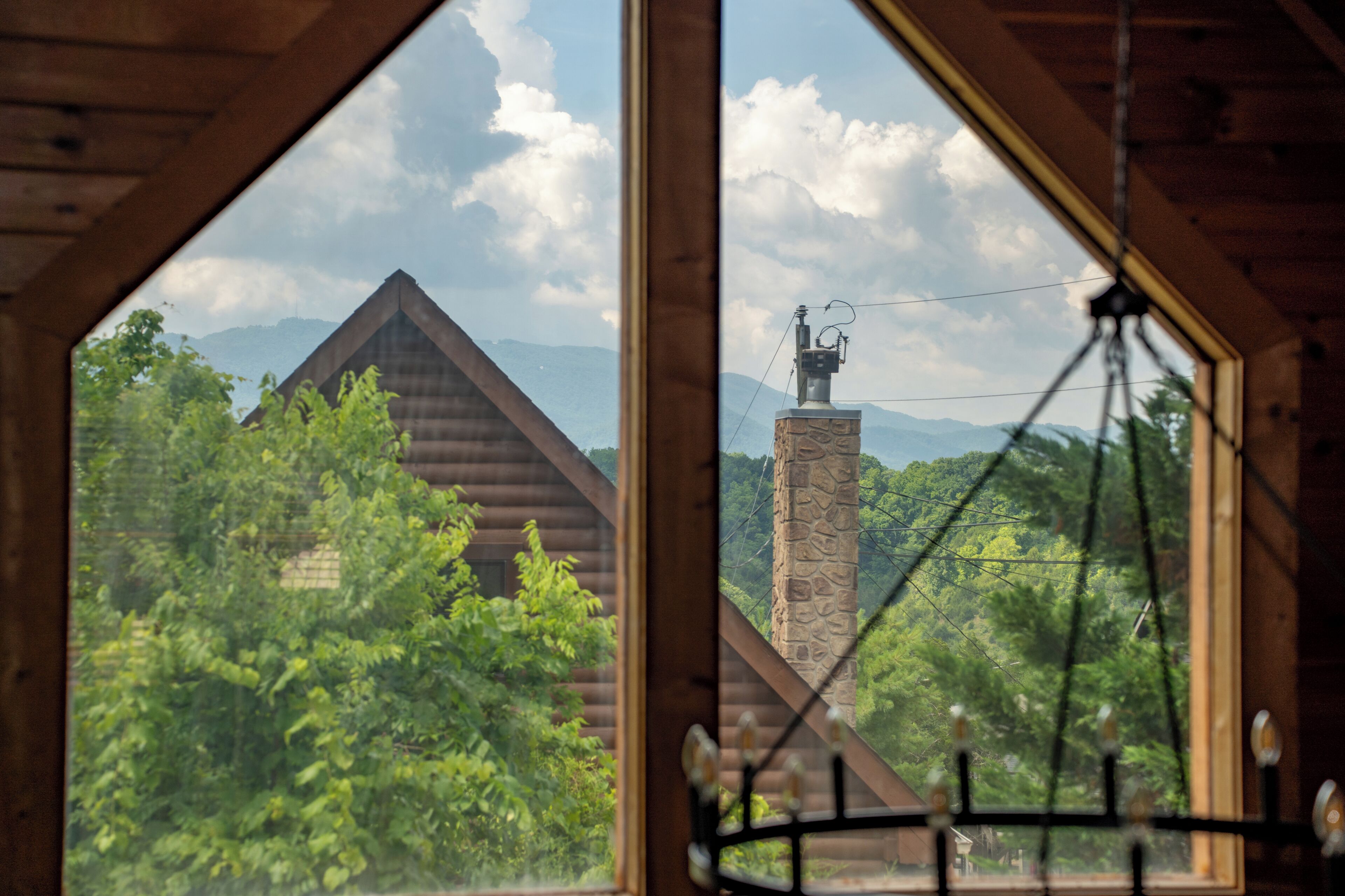 A view through a window with a wooden interior, overlooking a mountain and a stone structure with a weather vane.