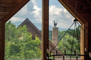 Vista per una finestra amb interior de fusta, amb una muntanya i una construcció de pedra amb un gallet nàutic.