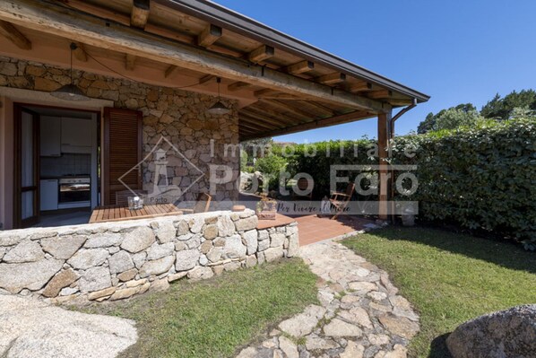 Une maison en pierre avec un porche en bois, un mur de pierre et une cour gazonnée.