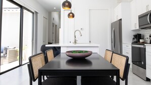 Une cuisine moderne avec un coin repas, comprenant une grande table, des chaises et des luminaires suspendus.