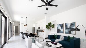 Un salon moderne avec un canapé, une table basse et des fauteuils. On aperçoit à l’arrière-plan un coin repas avec une table et des chaises.