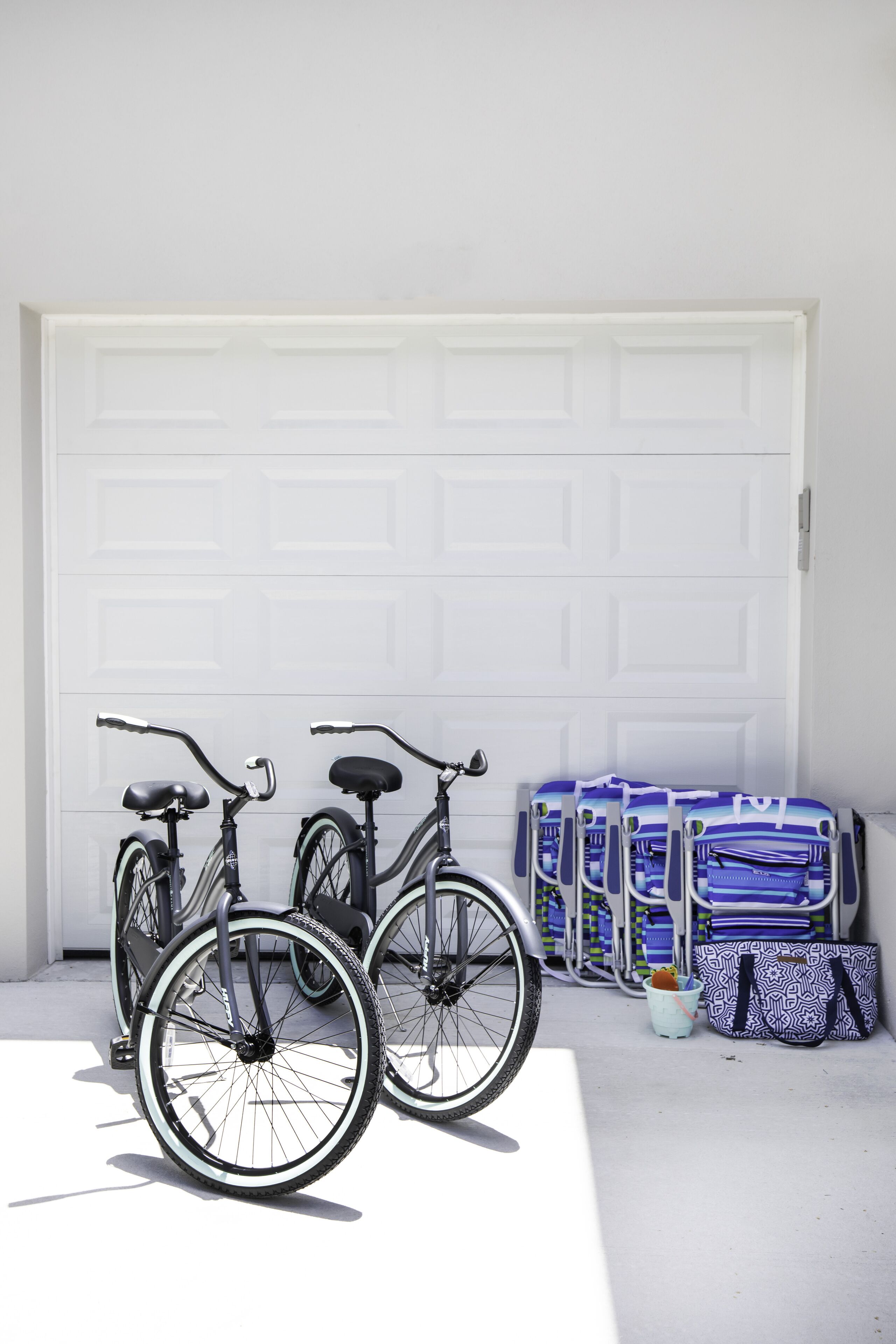 Two bicycles parked in front of a white garage door, with several bags and a bucket nearby.