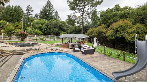 Une piscine avec un toboggan, un espace barbecue et une terrasse en bois.