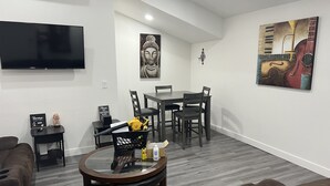 Un salon moderne avec une table basse ronde en verre, un canapé, une table à manger avec des chaises, un téléviseur à écran plat fixé au mur et des œuvres d’art accrochées aux murs.