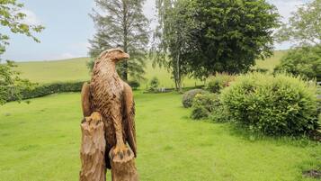 Une sculpture d’aigle en bois, située dans un espace extérieur verdoyant, agrémenté d’arbres et d’arbustes.