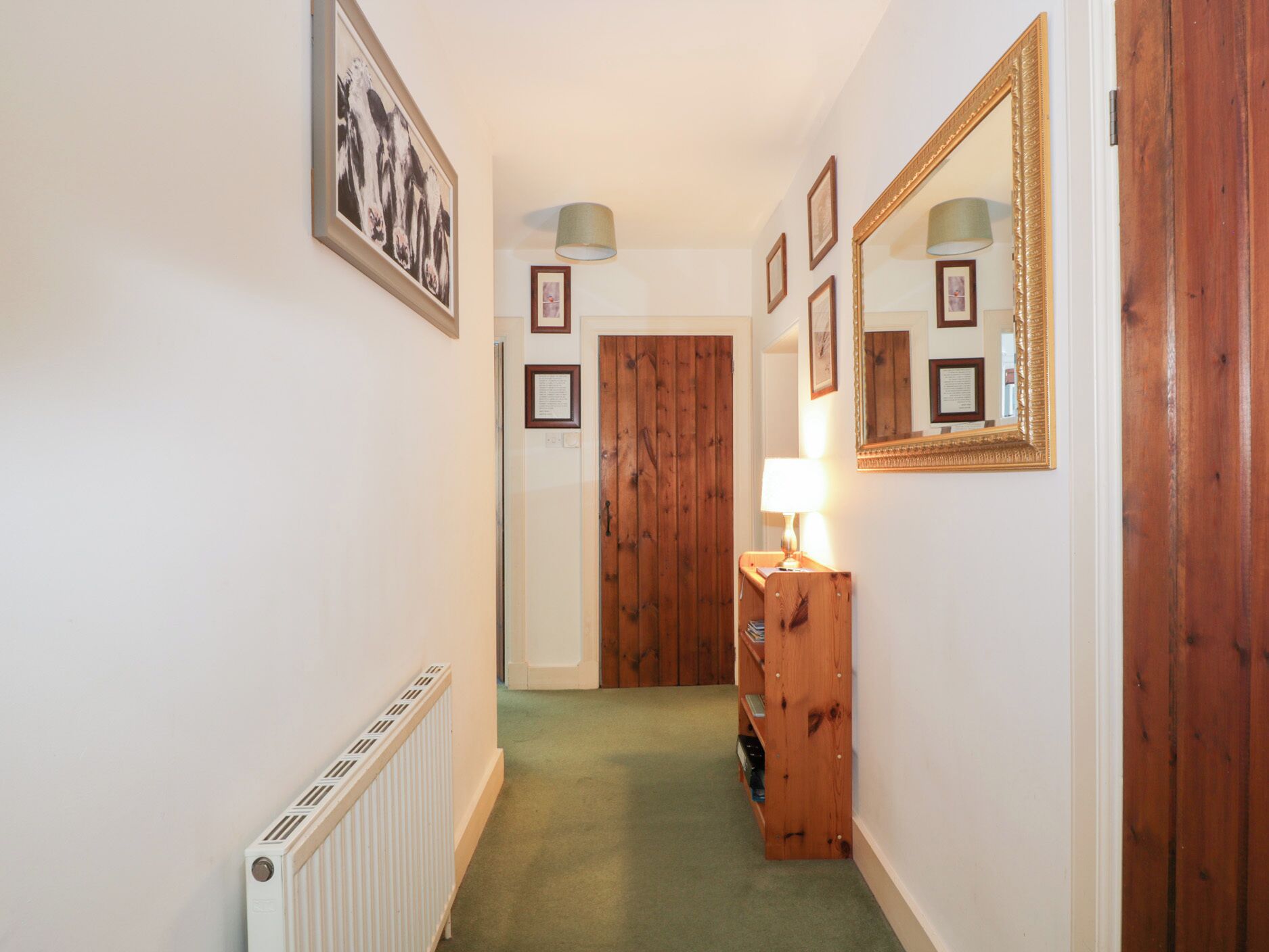 A hallway with a radiator, wooden door, and a lamp on a wooden cabinet.