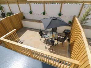 Un patio in legno con tavolo e sedie, un barbecue e luci a catena.