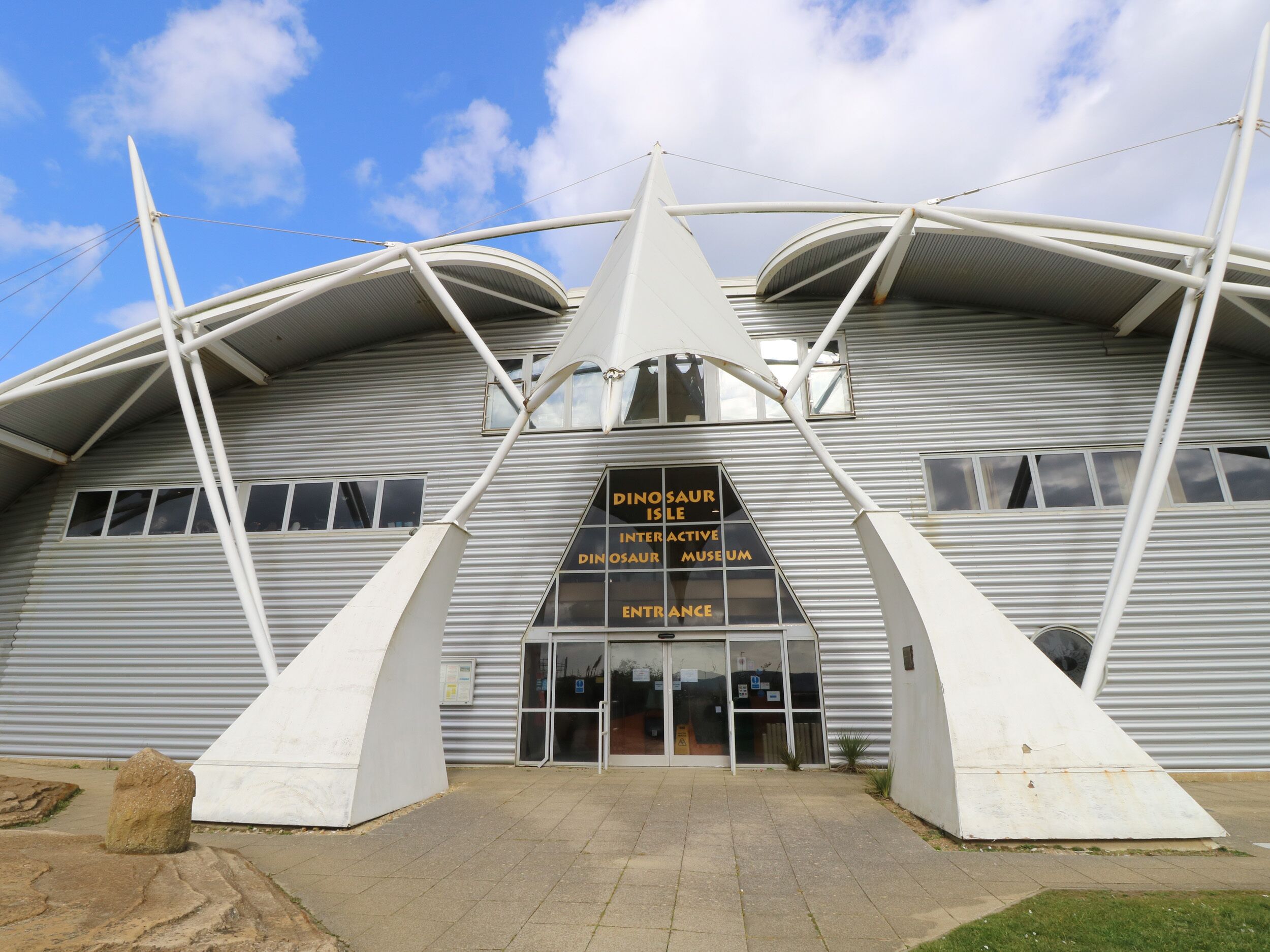 A modern building with a unique architectural design, featuring a prominent entrance and signage for the Dinosaur Isle Interactive Dinosaur Museum.