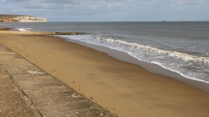 Une plage de sable avec une promenade en béton et une falaise en arrière-plan.