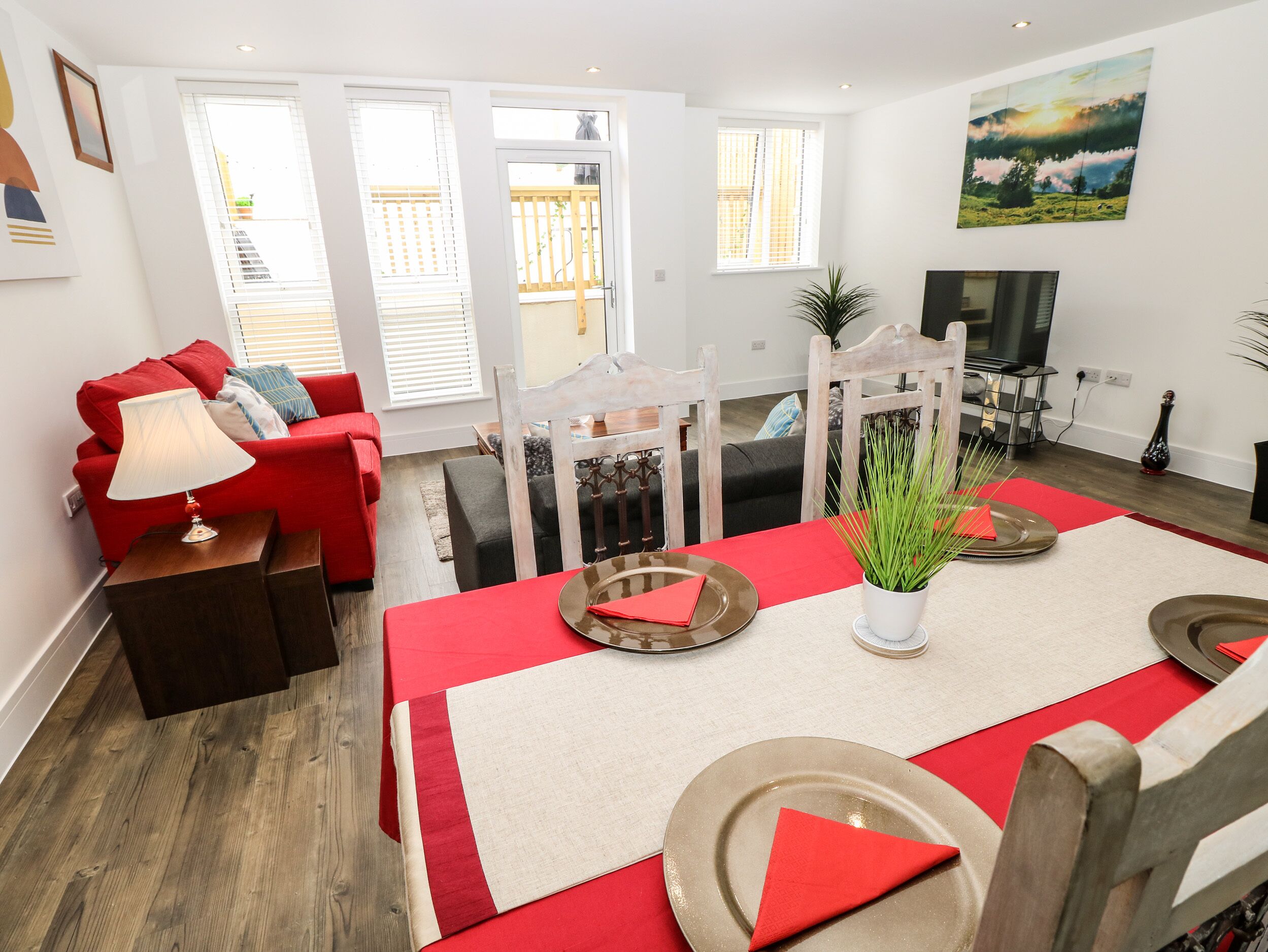 A modern living room with a red sofa, a dining table set for four, and a TV in the background.