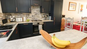 Une cuisine moderne avec des meubles de couleur sombre, un four encastré et une table à manger en bois sur laquelle se trouvent des bananes.