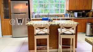 A kitchen with wooden cabinets, a stainless steel refrigerator, a microwave, and a window with a view of greenery. - PARADISE VILLA  CHEF+FOOD GOLF POOL BBQ KING BEDS (Juan Dolio)