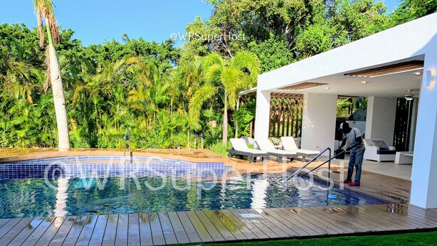 A modern outdoor pool area with a wooden deck, a small pool, and a covered seating area with lounge chairs. - PARADISE VILLA  CHEF+FOOD GOLF POOL BBQ KING BEDS (Juan Dolio)